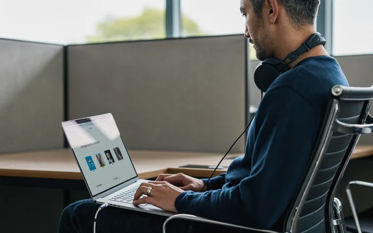 A man working through a course on a laptop at a quiet desk, headphones around his neck.