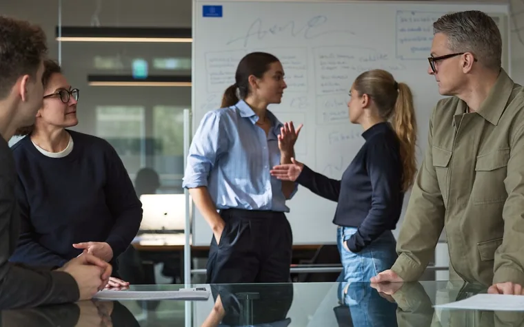 Four colleagues around a meeting table, working through a plan on a whiteboard behind them